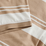 Close-up of beige and white striped fabric from the Fundamental Engineered Stripe Polo by Canterbury, showing a sleeve and hem with visible stitching.