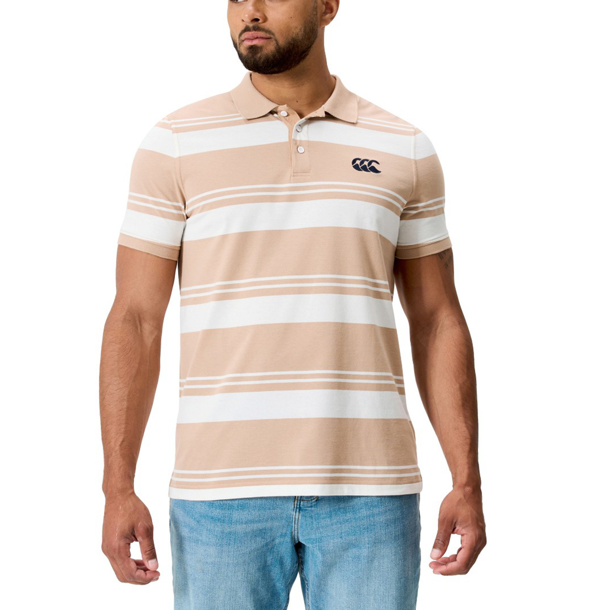 A man wearing the Fundamental Engineered Stripe Polo by Canterbury in beige and white with a small chest logo, paired with light blue jeans.