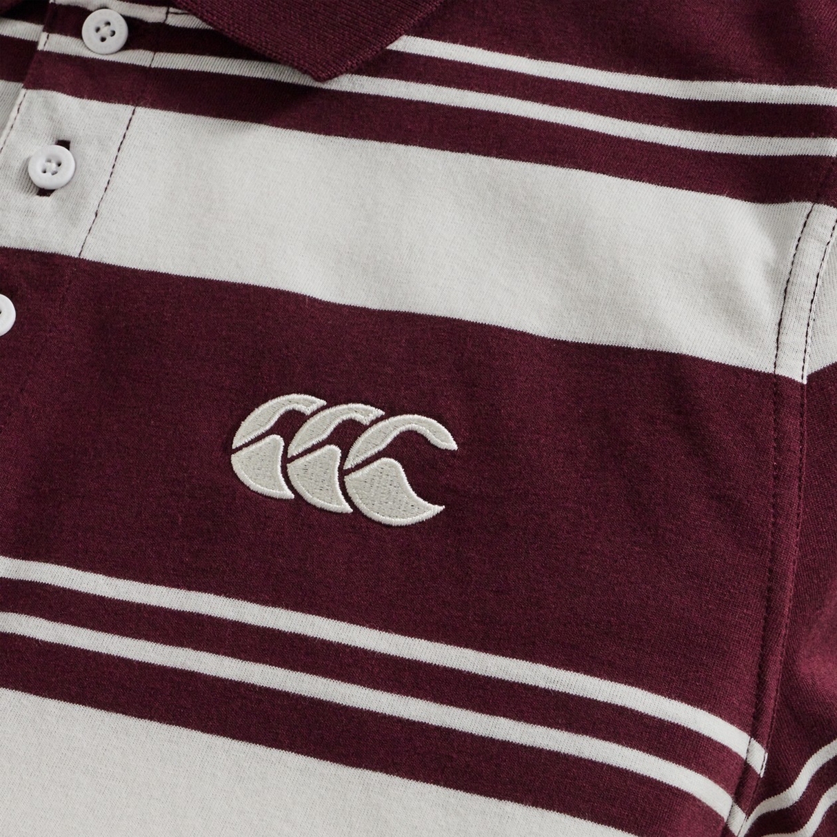 Close-up of the Fundamental Engineered Stripe Polo by Canterbury in maroon and white, highlighting its rugby heritage with an embroidered white Canterbury logo on the chest.