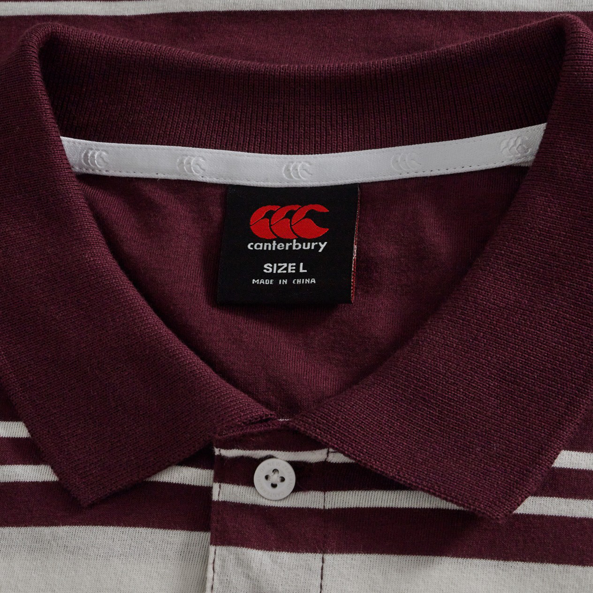 Close-up of the Fundamental Engineered Stripe Polo by Canterbury in maroon and white, size L, featuring a visible Canterbury brand label and white button below the collar—perfect for rugby polo fans.