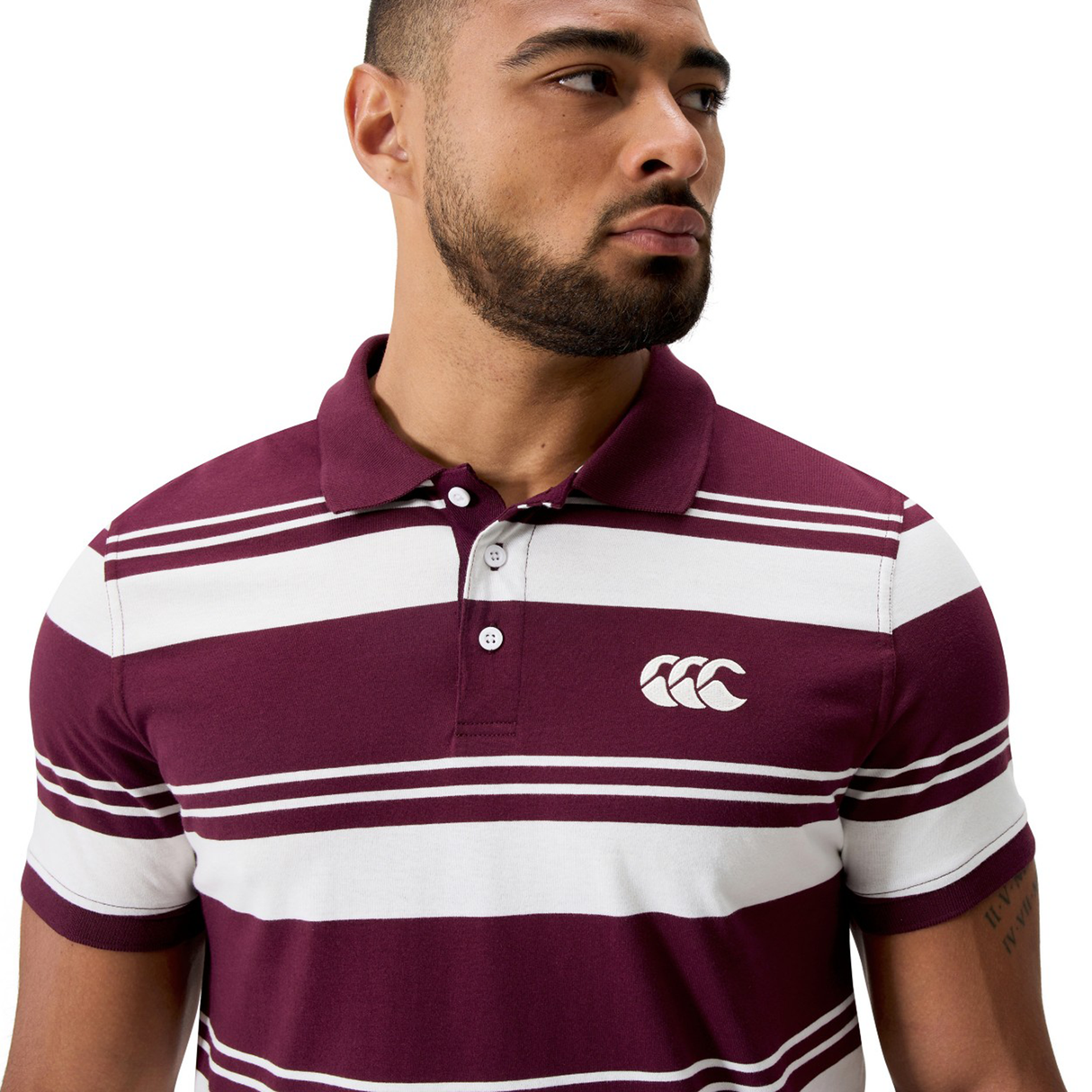 A man looks to his left against a white background wearing the Canterbury Fundamental Engineered Stripe Polo in maroon and white, featuring engineered stripes and a chest logo.