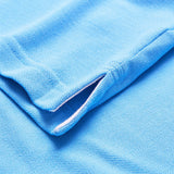 Here’s a revised version using the product data: Close-up of a light blue textured fabric from the Canterbury by Canterbury Solid Dye Polo, highlighting a small side slit and precise stitching along the seam.