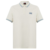 The Canterbury Fundamental Solid Dye Polo is cream-colored with a rugby-inspired look, featuring blue and white striped collar and cuffs, plus a blue logo on the left chest.