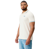 Man in a Canterbury Fundamental Solid Dye Polo—cream with blue trim—and light blue jeans, standing against a white background.