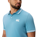 A man wearing Canterbury’s Fundamental Solid Dye Polo—a light blue, short-sleeve shirt with white trim and a white chest logo.