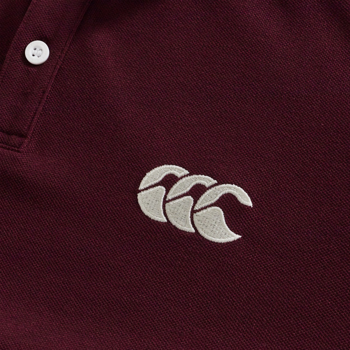 Close-up of the Canterbury Fundamental Solid Dye Polo in maroon, featuring two white buttons and a white embroidered Canterbury logo on the chest, highlighting its rugby-inspired style.