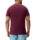A man is shown from the back wearing Canterbury’s Fundamental Solid Dye Polo in maroon with white trim and light blue jeans, showcasing a subtle rugby-inspired design.