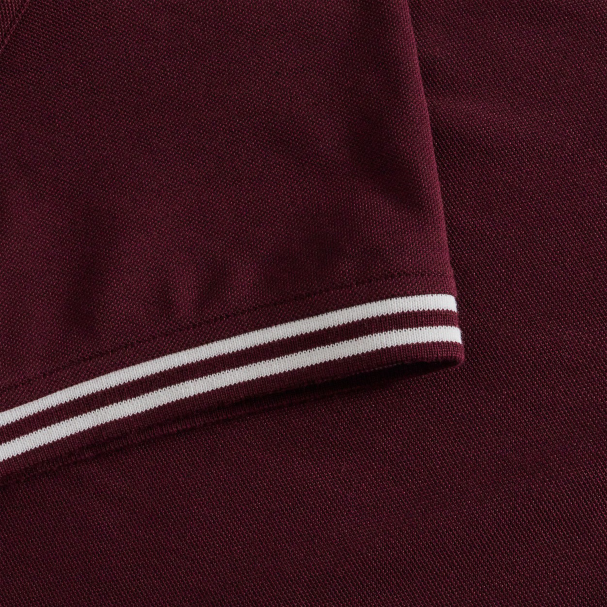 Close-up of the Canterbury Fundamental Solid Dye Polo, a maroon short-sleeve shirt featuring white and maroon double stripes on the sleeve cuffs for a rugby-inspired look.
