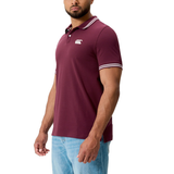 A man in the Canterbury Fundamental Solid Dye Polo, featuring white striped details and paired with light blue jeans, stands against a white background, showcasing this rugby-inspired Canterbury design.