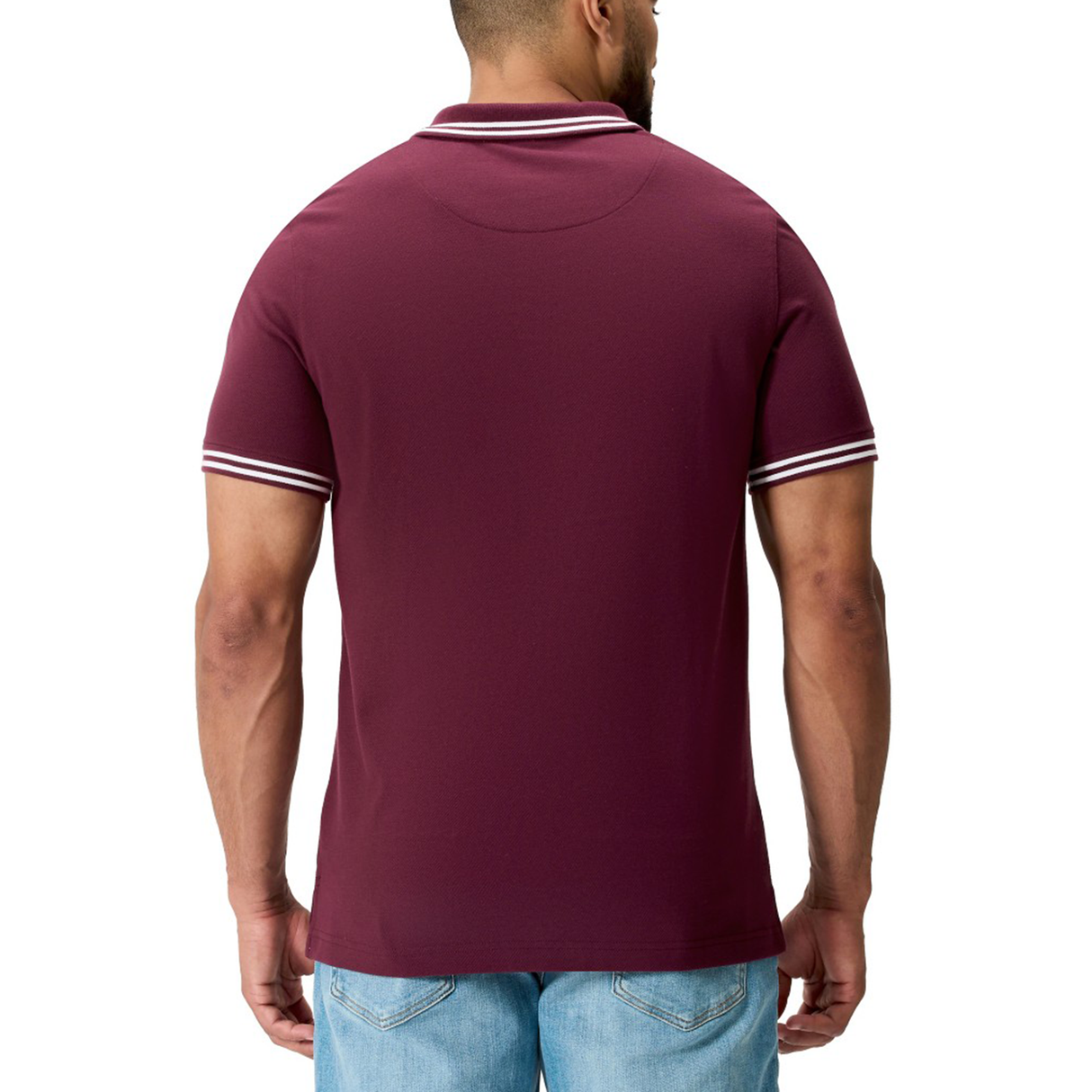 A man is seen from the back wearing the Canterbury Fundamental Solid Dye Polo, a maroon rugby-inspired shirt with white collar and sleeve trim, paired with light blue jeans.