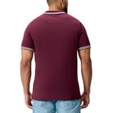 A man is seen from the back wearing the Canterbury Fundamental Solid Dye Polo, a maroon rugby-inspired shirt with white collar and sleeve trim, paired with light blue jeans.