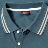Close-up of the Canterbury Solid Dye Polo, a teal rugby-inspired shirt by Canterbury, featuring beige stripes on the collar, two white buttons, and a visible black brand tag under the collar.