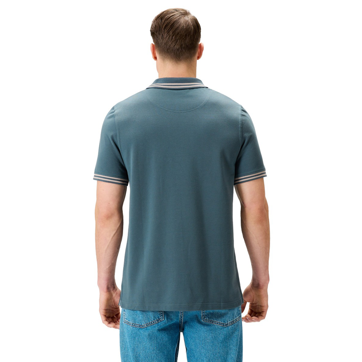 A man stands with his back to the camera, wearing a Canterbury Solid Dye Polo and blue jeans against a plain white background.