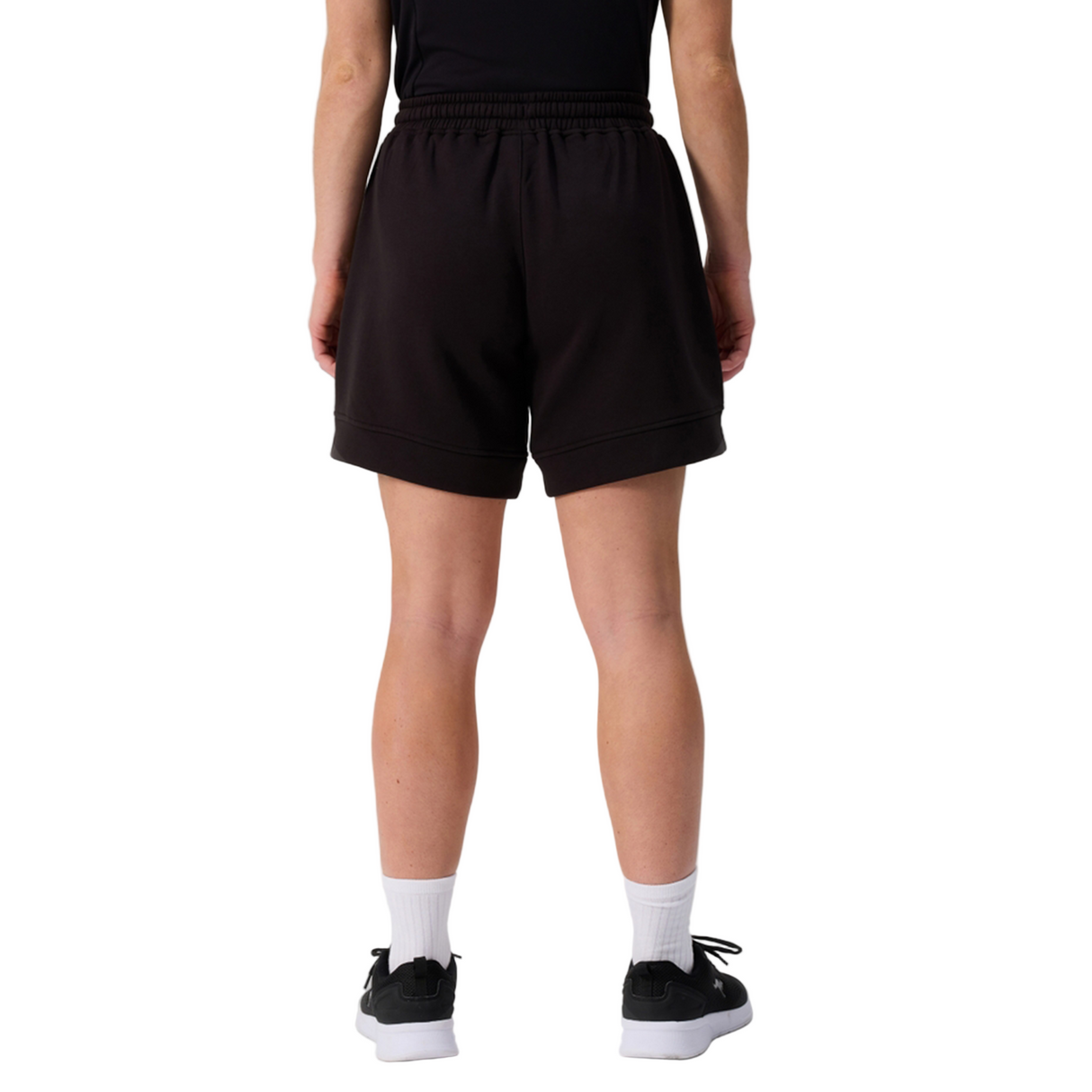 A person shown from the waist down, facing away, wears Canterbury Women's Ireland 25/26 Knit Short, a black shirt, white socks, and black sneakers against a white background.