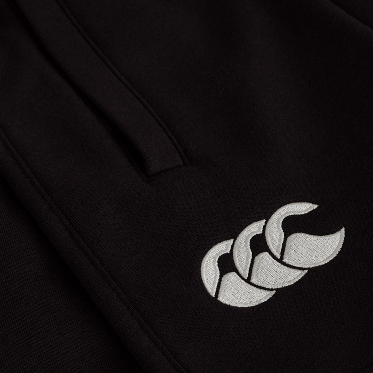 Close-up of the Women's Ireland 25/26 Knit Short by Canterbury, showing a white embroidered triple-shape logo on black fabric. Perfect addition to women's sports shorts collections.