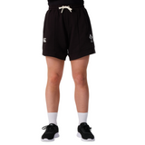 A person stands against a white background, showing only the lower half while wearing Canterbury Women's Ireland 25/26 Knit Shorts, paired with white socks and black sneakers—highlighting these stylish sports shorts by Canterbury.