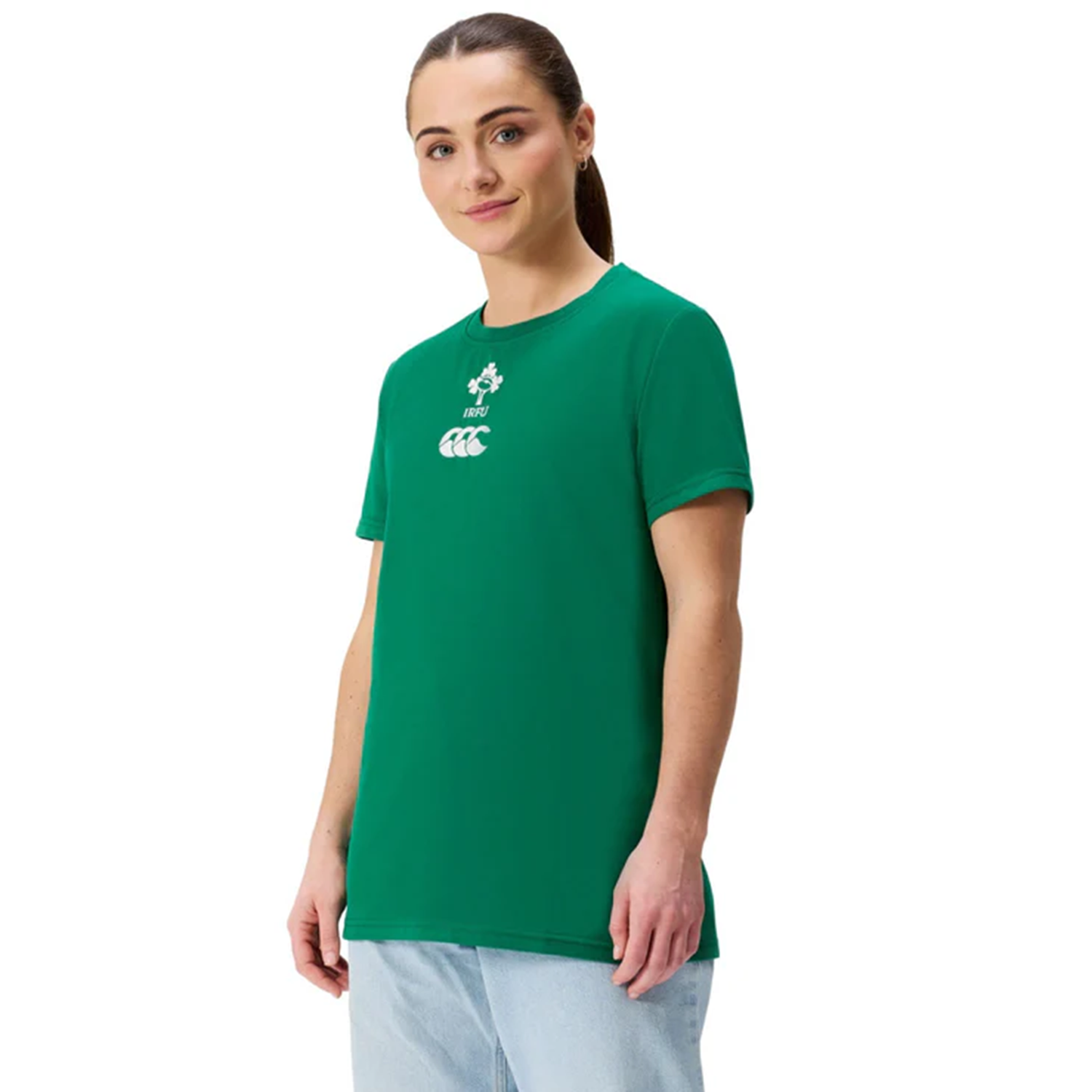 A person in the Women's Ireland 25/26 Cotton Team T-Shirt by Canterbury with white logos, paired with light blue jeans, stands against a plain white background.