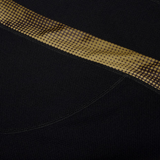 Close-up of the black textured fabric from the Canterbury Tempo+ Drill Top, featuring a diagonal strip with a gold and brown dotted pattern.