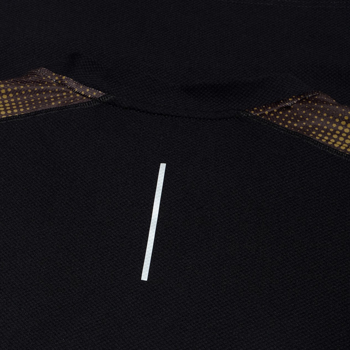 Close-up of the black Tempo+ Drill Top by Canterbury, featuring a central vertical reflective strip and brown patterned mesh accents—moisture-wicking and ideal for performance training.
