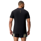 A man faces away, wearing the Canterbury Tempo+ Drill Top—a black moisture-wicking performance training top with a vertical back line—and black shorts featuring a yellow pattern.