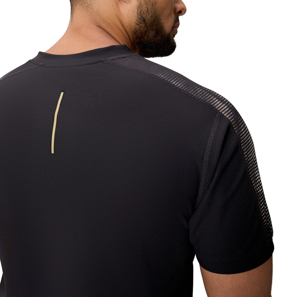 A man is seen from behind wearing the Canterbury Tempo+ Drill Top, a black performance training top with a small vertical beige stripe on the upper back. Made from moisture-wicking fabric for comfort during workouts, photographed against a white background.