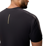 A man is seen from behind wearing the Canterbury Tempo+ Drill Top, a black performance training top with a small vertical beige stripe on the upper back. Made from moisture-wicking fabric for comfort during workouts, photographed against a white background.
