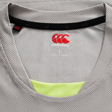 Close-up of the neckline on a gray Tempo+ Drill Top by Canterbury, featuring the brand logo, size "L" label, and a glimpse of yellow moisture-wicking sportswear fabric underneath.