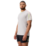 A man stands against a white background wearing the Canterbury Tempo+ Drill Top in light gray, made from moisture-wicking fabric, and black shorts, looking at the camera.