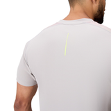 A man shown from behind wears the Canterbury Tempo+ Drill Top, a light grey textured rugby top featuring moisture-wicking technology and a single vertical yellow stripe on the upper back.
