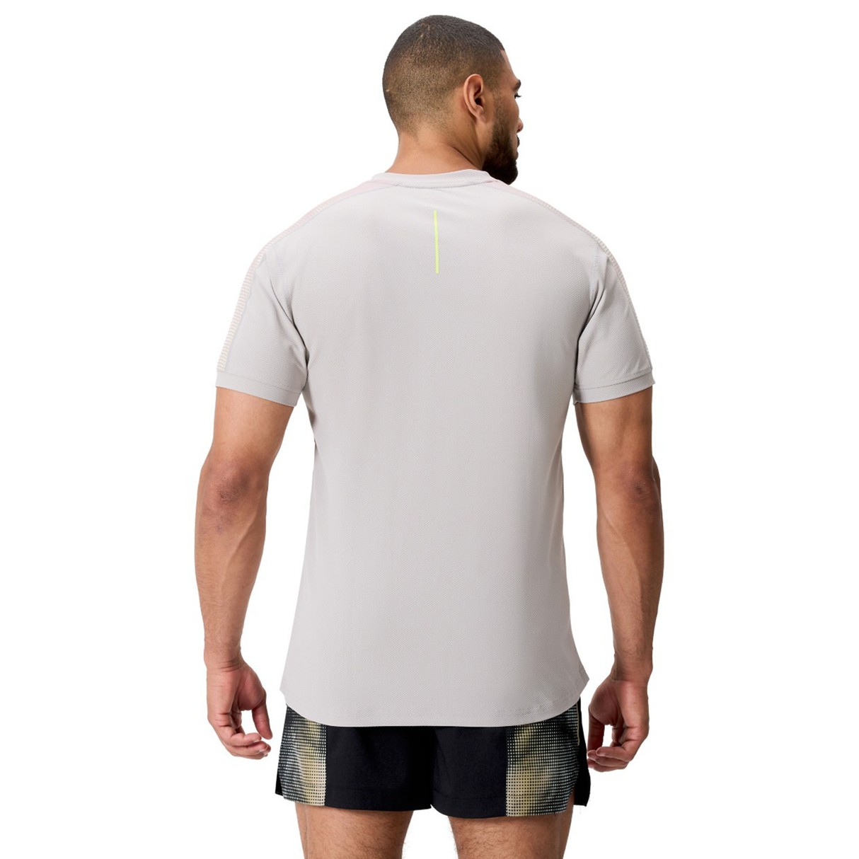 A man faces away from the camera, wearing the Canterbury Tempo+ Drill Top in light gray with moisture-wicking fabric and black shorts, set against a plain white background.