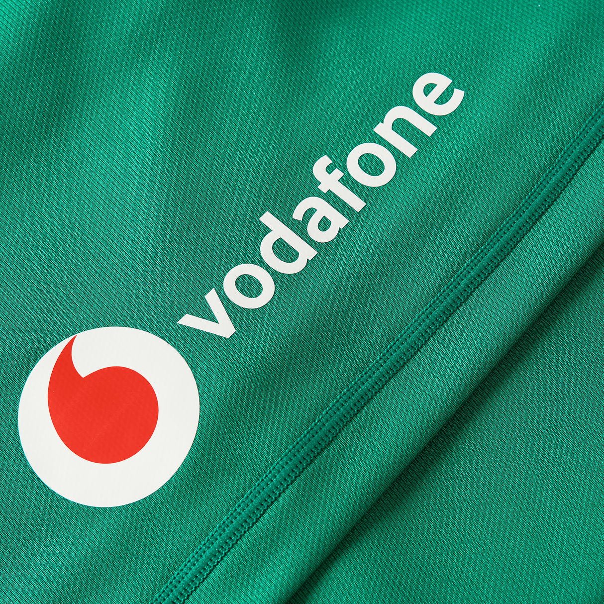 Close-up of green fabric from the Women's Ireland WIRFU 25/26 Pro Home Jersey by Canterbury, showing white Vodafone text and logo with a red-and-white circular emblem.