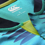 Close-up of the Ireland 26 Pre Game Pro Jersey by Canterbury in teal and black, highlighting the signature logo, size label, embroidered seams, and a section of striking printed pattern. This moisture-wicking Canterbury sports jersey combines detailed construction with high-performance style.