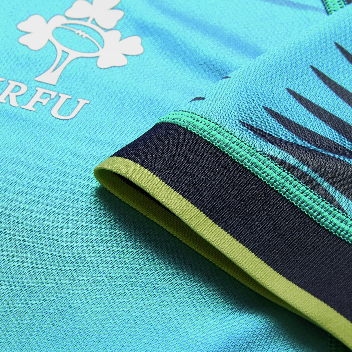 Close-up of the Ireland 26 Pre Game Pro Jersey by Canterbury, showcasing its turquoise color with black and green trim, a logo featuring a shamrock and rugby ball alongside the letters “IRFU.” This Canterbury jersey is designed as a moisture-wicking sports top for optimal comfort on or off the field.