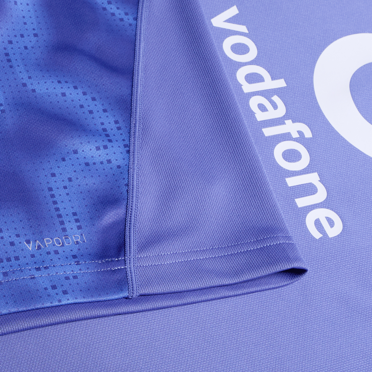 Close-up of the Ireland 25/26 Six Nations Pro Training Jersey by Canterbury in purple, showing the "VAPODRI" label, placed beside a mat with "vodafone" printed in white letters.