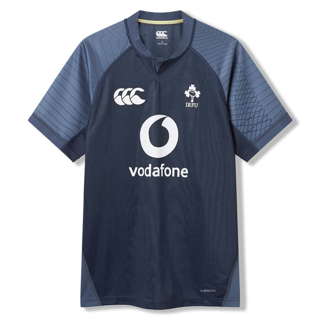 The Ireland 26 Training Pro Jersey by Canterbury is a navy blue rugby top with short sleeves, Vodafone sponsor, and IRFU chest logo, featuring patterned shoulder panels. Displayed on a white background, this Canterbury jersey is crafted with innovative VapoDri fabric for superior comfort and performance.