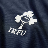 The Ireland 26 Training Pro Jersey by Canterbury features the IRFU logo—a shamrock and rugby ball design—printed in white on dark blue textured fabric, and incorporates Canterbury’s signature VapoDri technology for optimal comfort.