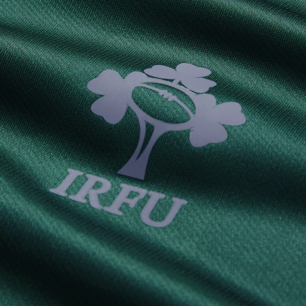 A close-up of the IRFU logo printed on dark green fabric, featured on the Ireland 26 Training Pro Jersey by Canterbury. The emblem displays a shamrock above a rugby ball with the “IRFU” acronym beneath, highlighting the official design present on every authentic Canterbury Ireland Rugby Jersey.