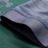 Close-up of the gray hem on the Ireland 26 Training Pro Jersey by Canterbury, shown lying over a green textile adorned with subtle white printed motifs and fine stripes—details reminiscent of Canterbury’s signature VapoDri technology featured in their training jerseys.