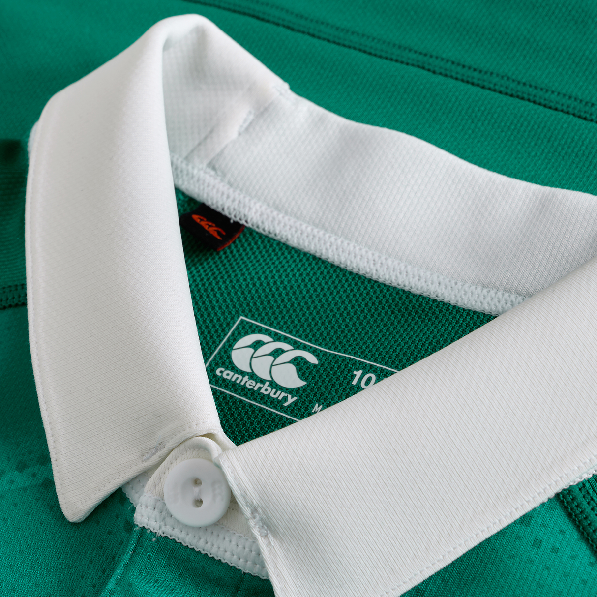 Close-up of the Canterbury Youth Ireland 25/26 Home Pro Jersey in green, featuring a white collar with button, visible brand logo, and size label.