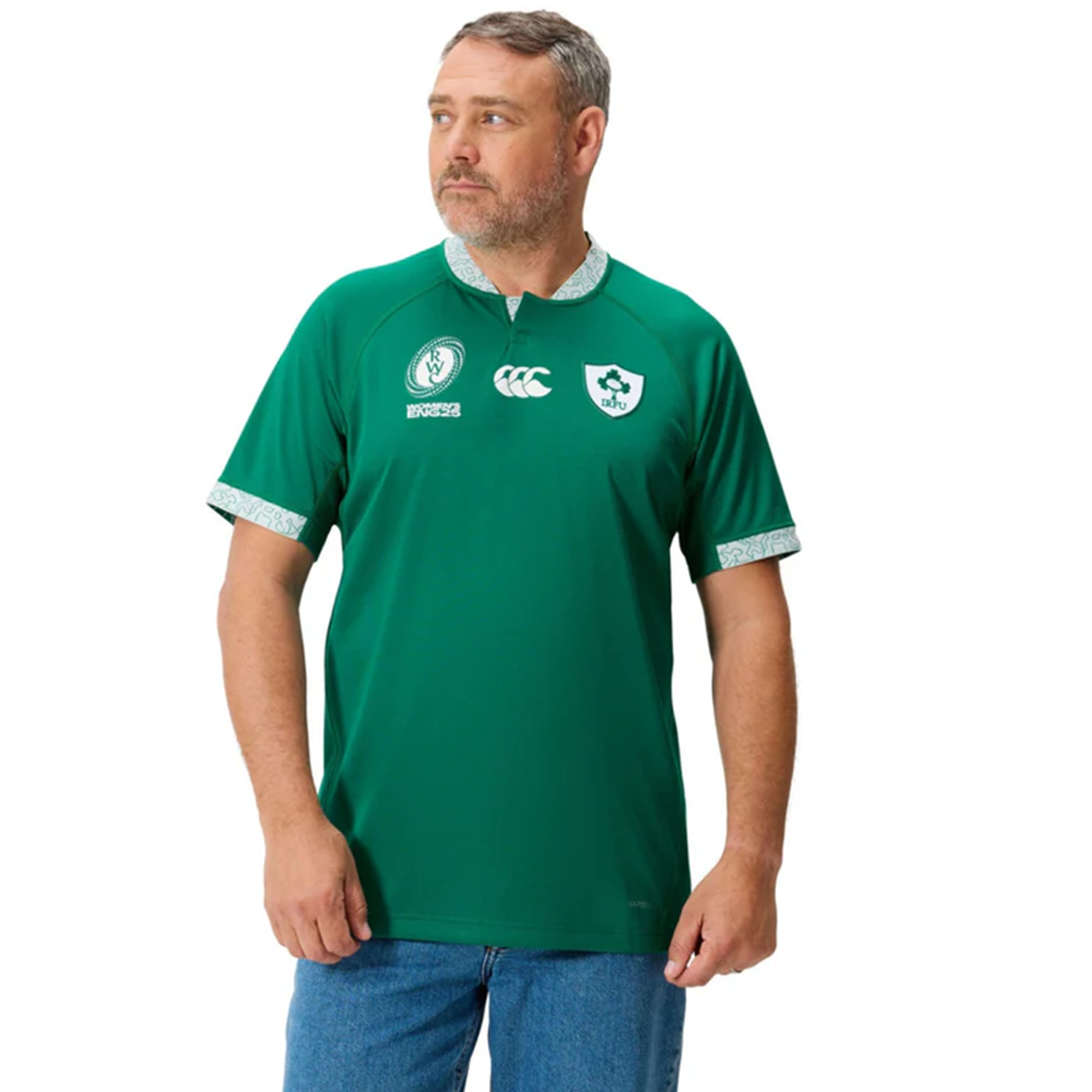 A man wears the Ireland WRWC25 Replica Home Jersey by Canterbury with blue jeans, standing slightly sideways against a white background.