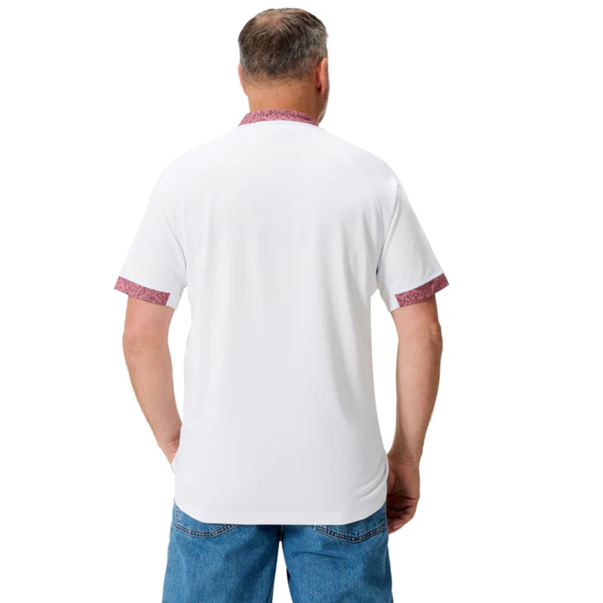 A man in a white Ireland WRWC25 Replica Alternate Jersey by Canterbury, featuring patterned red trim, and blue jeans stands with his back to the camera.