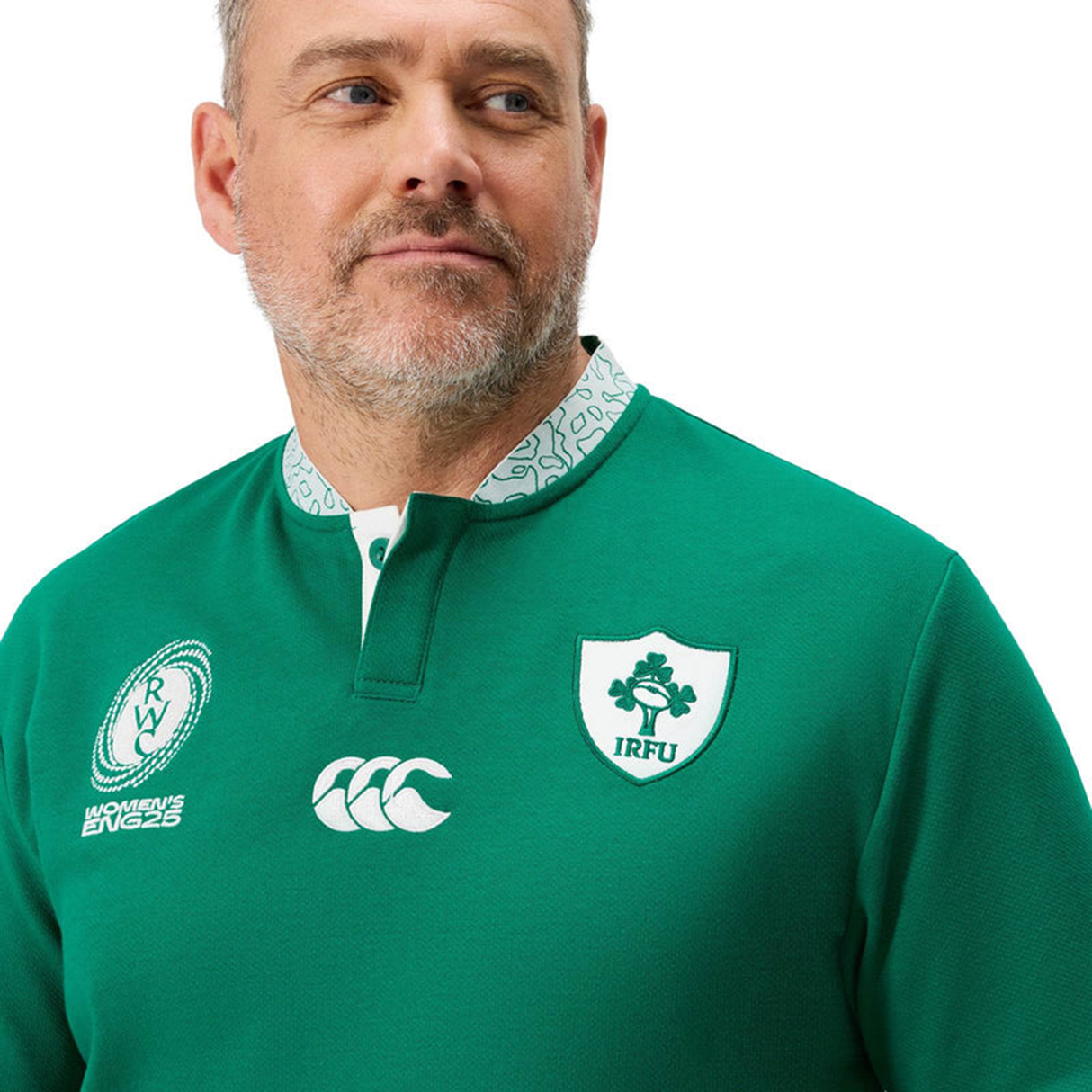 A man wearing the Ireland WRWC25 Classic Jersey by Canterbury, featuring IRFU and Canterbury logos, looks to the side against a white background. This Canterbury jersey showcases timeless style and Irish pride.