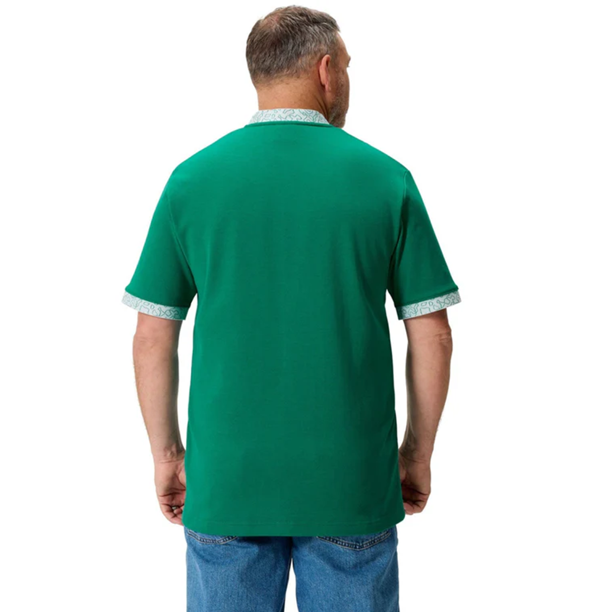 A man wearing the Ireland WRWC25 Classic Jersey by Canterbury, featuring green fabric with patterned cuffs and collar, and blue jeans, stands with his back to the camera.