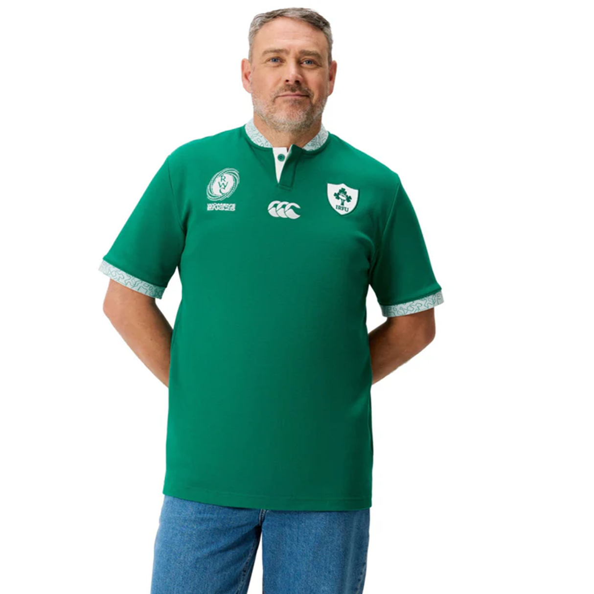 A man wearing blue jeans and the Ireland WRWC25 Classic Jersey by Canterbury, featuring logos, stands against a white background.