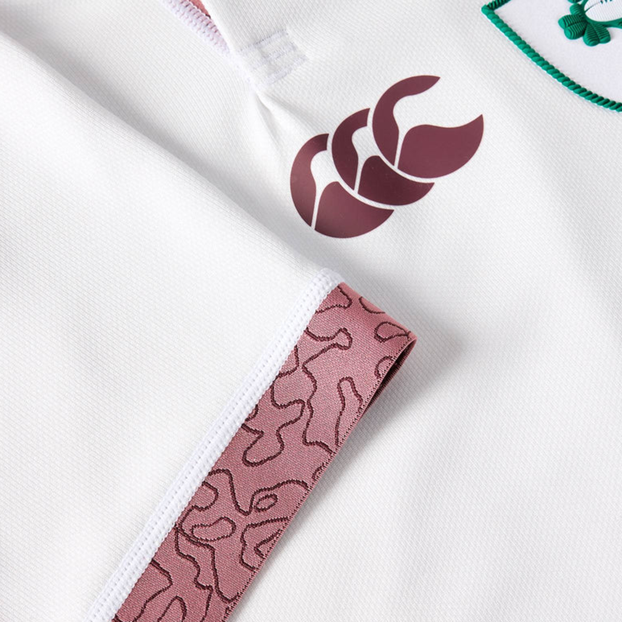 Close-up of the Women's Ireland WRWC25 Replica Alternate Jersey by Canterbury, showing a maroon logo, a patterned pink tag, and part of an embroidered green and white badge.