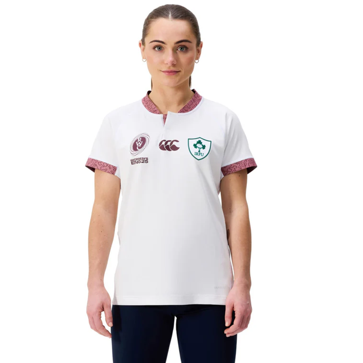 A woman stands facing forward, wearing the Women's Ireland WRWC25 Replica Alternate Jersey by Canterbury—a white rugby jersey with maroon accents and multiple chest logos.