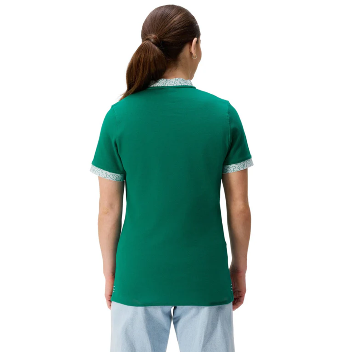 A woman with long brown hair in a ponytail stands facing away, wearing the Canterbury Women's Ireland WRWC25 Classic Jersey with patterned trim and light blue pants.