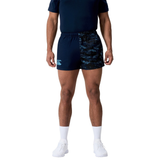 A person wearing a navy Canterbury athletic outfit with Force Harlequin Drill Shorts by Canterbury, white socks, and white sneakers stands against a plain background.