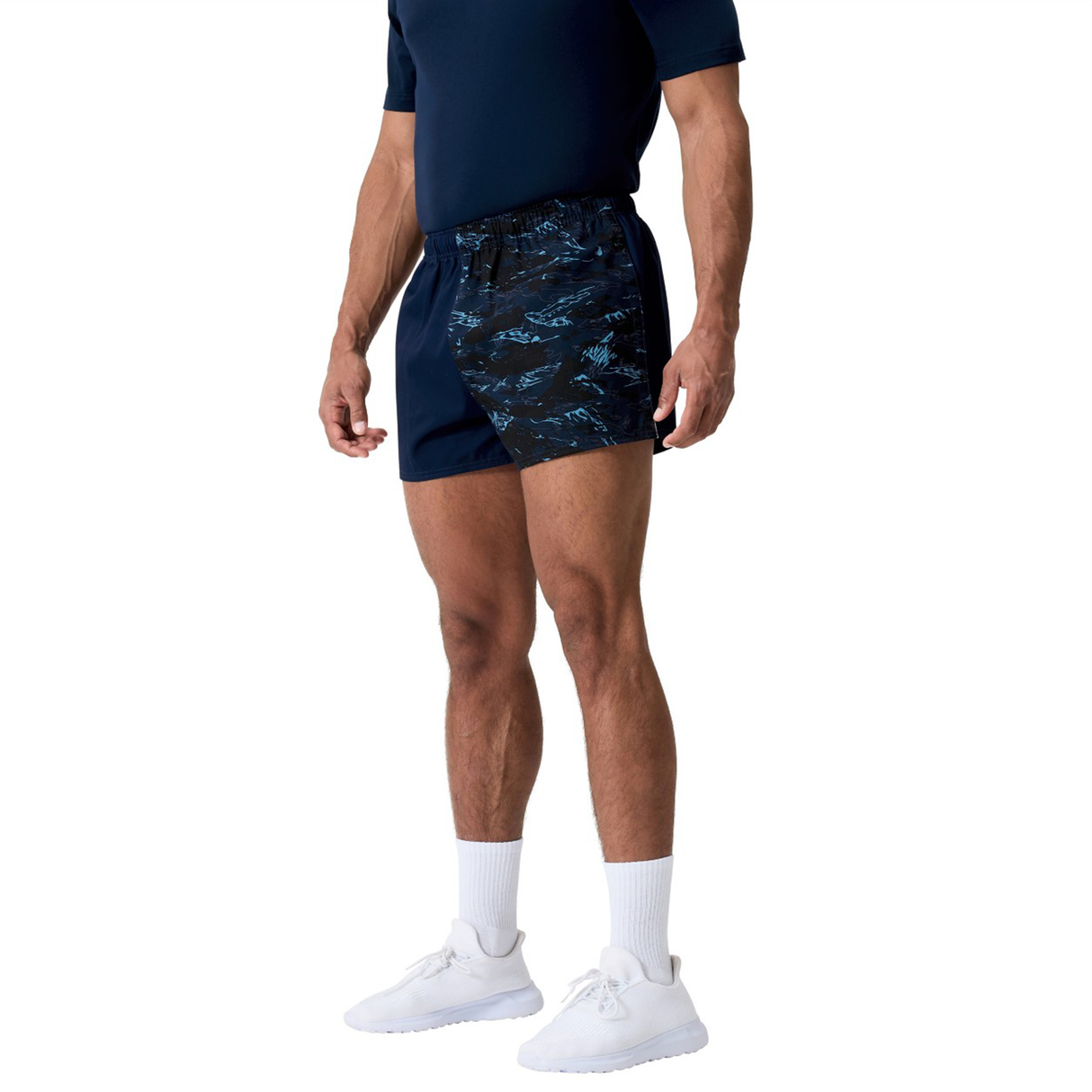 A man in a navy blue t-shirt, Canterbury Force Harlequin Drill Shorts, white socks, and white athletic shoes stands against a plain background.