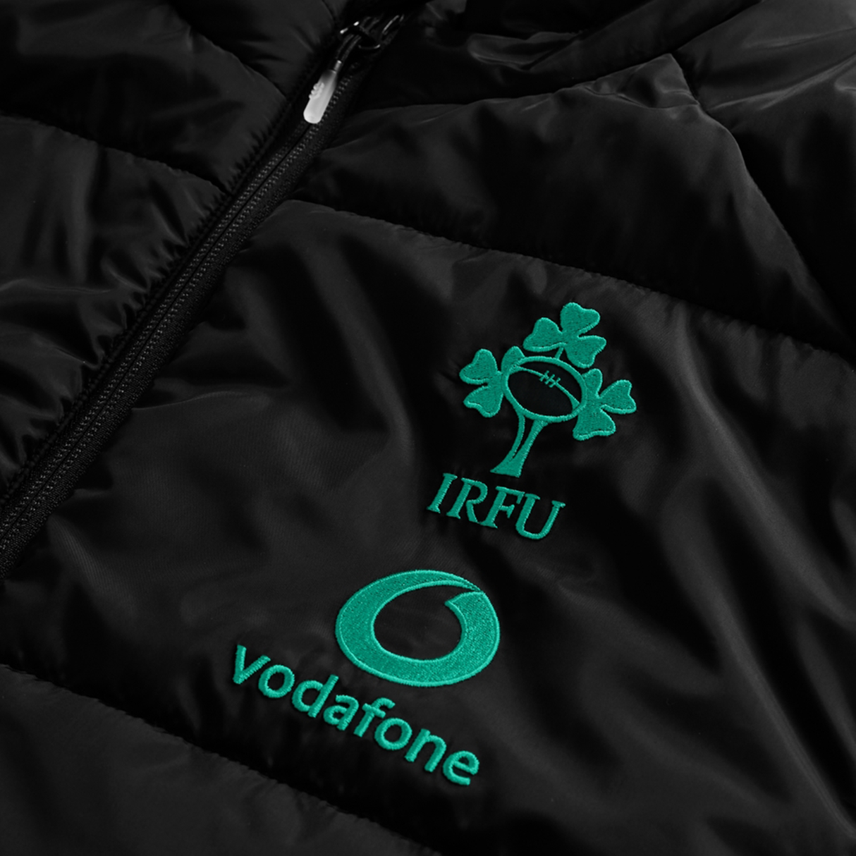 Close-up of the Ireland 25/26 Elite Gilet by Canterbury, showcasing embroidered IRFU and Vodafone logos in green on a black jacket.